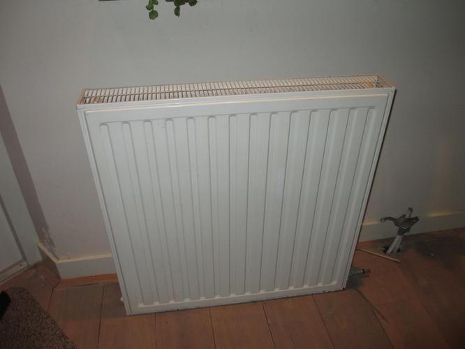 Een radiator aansluiten in woonkamer. In de uitbouw ligt ondergrond